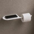 Wall-mounted toilet paper holder with smartphone tray in a bathroom setting.