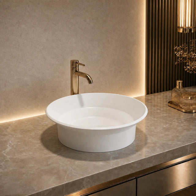 White round sink with gold faucet on a marble countertop in a bathroom setting.