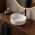 White solid surfaces sink on a wooden vanity with a black faucet and decorative items.